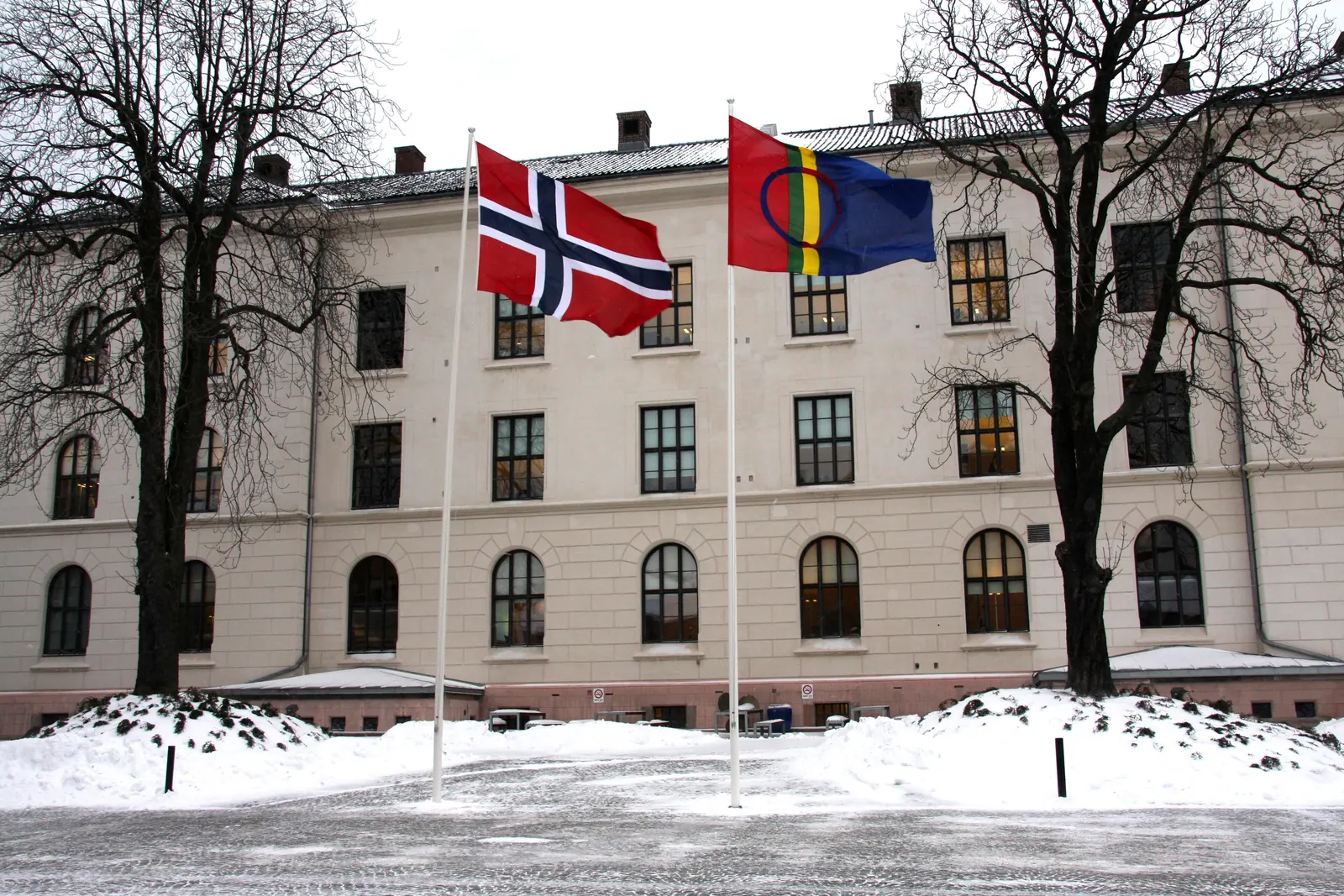 Norsk og samisk flagg på hver sin stang foran Statsministerens kontor en vinterdag
