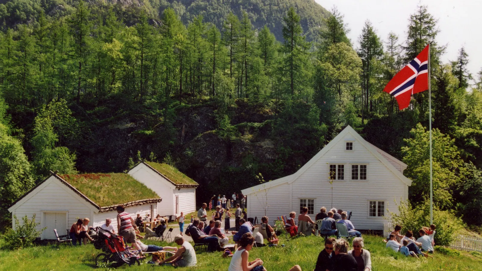 Hvite hus og en høy flaggstang med norsk flagg ved Ryfylkemuseet på Håland