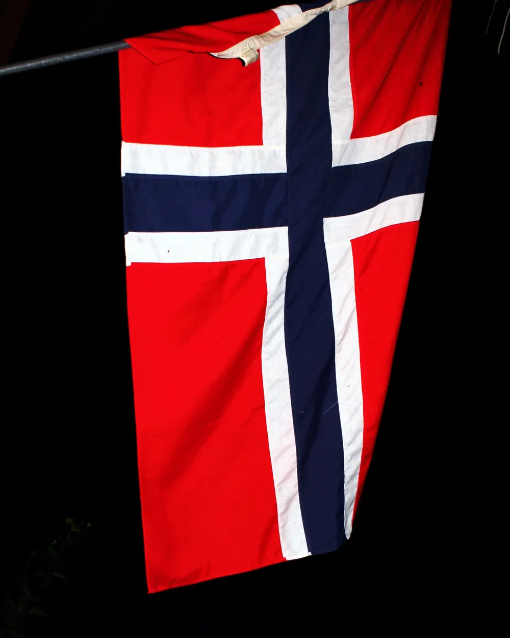 Et norsk flagg som henger rett ned mot svart bakgrunn