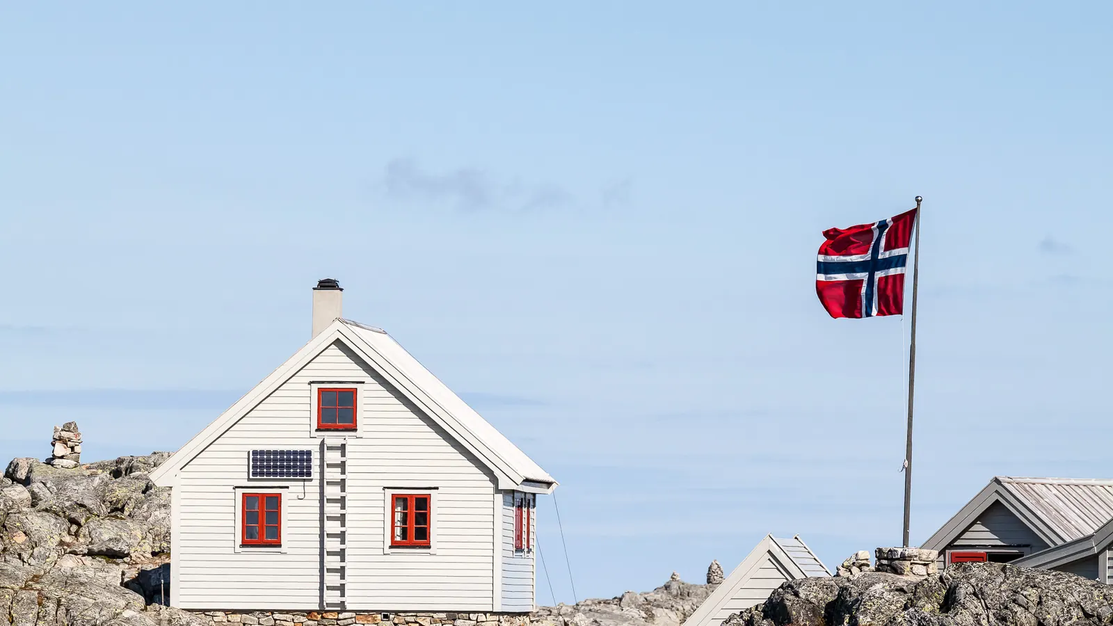 Hvitt hus på svaberg med norsk flagg på en hvit flaggstang i Kvinnherad