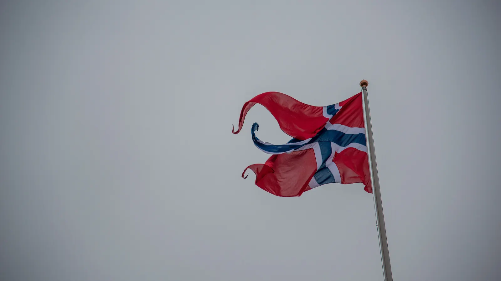 Et slitt og frynsete norsk flagg i vinden mot grå himmel