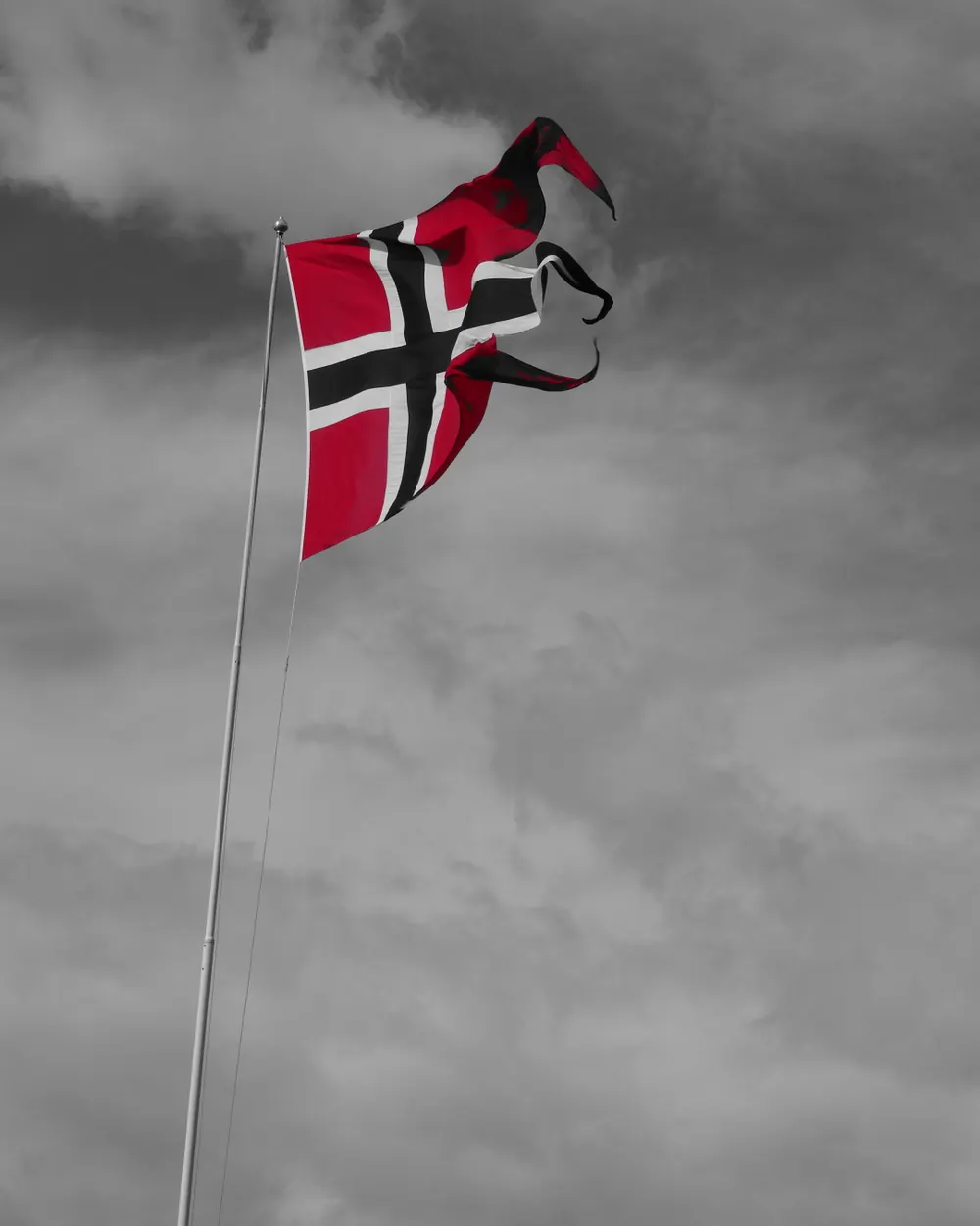Norsk flagg på stang mot grå skyer ved Vågen i Bergen