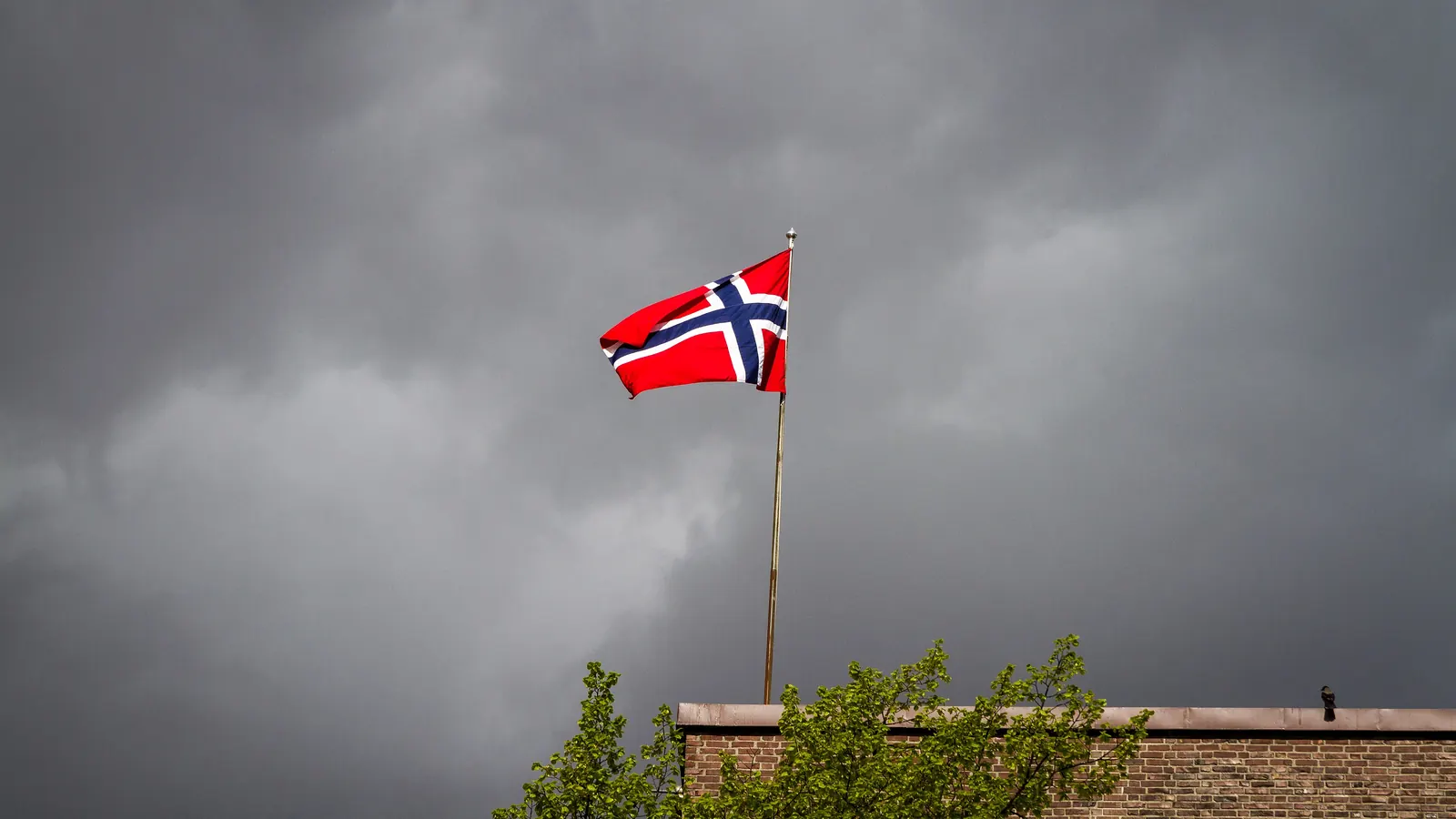 Norsk flagg på en stang under mørke regnskyer i Bergen