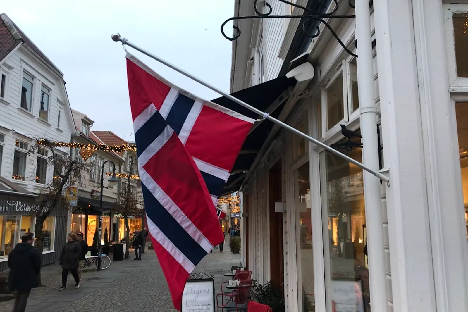 Norsk flagg på en skrå stang festet til husveggen i en handlegate i Stavanger