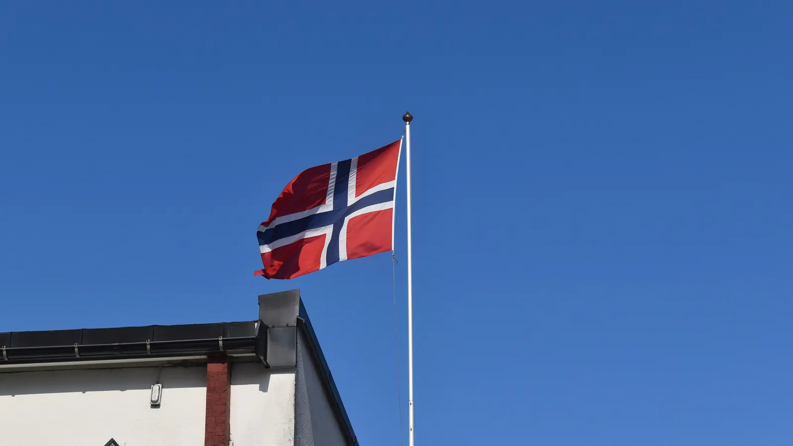 Norsk flagg på en flaggstang ved takkanten på et hvitt hus