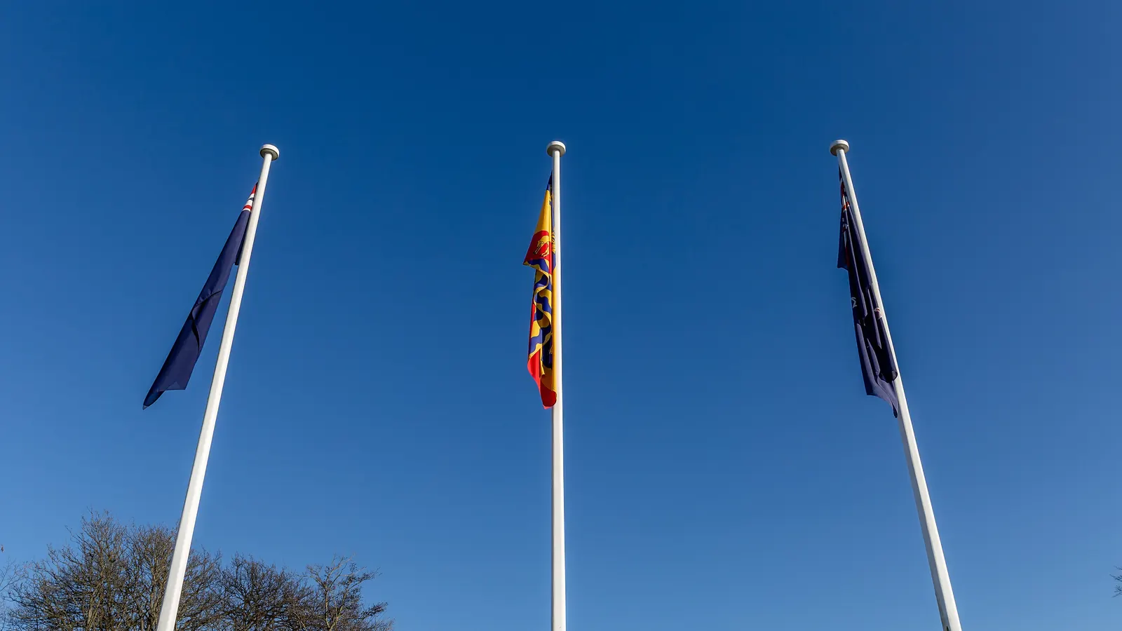 Three flagpoles with flags at a street corner in Christchurch