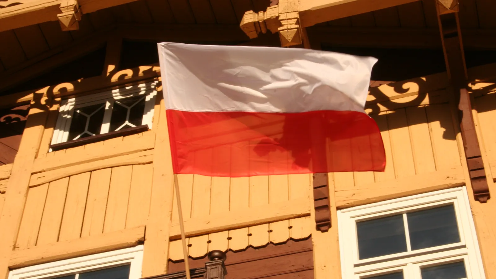 Flaga Polski na drzewcu w uchwycie na ścianie drewnianego domu