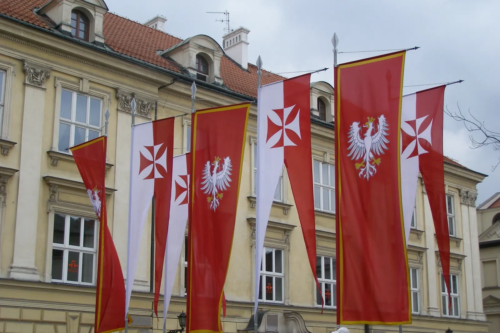 Pionowe flagi z godłem Polski na fasadzie budynku w Krakowie
