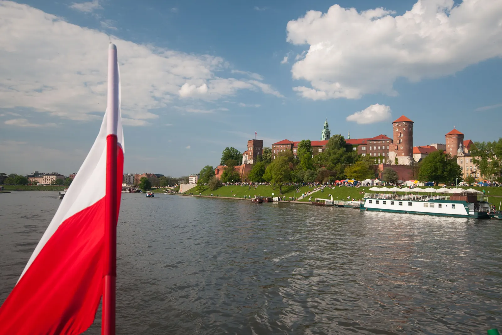Łódź z biało-czerwoną flagą na Wiśle, w tle Wzgórze Wawelskie w Krakowie
