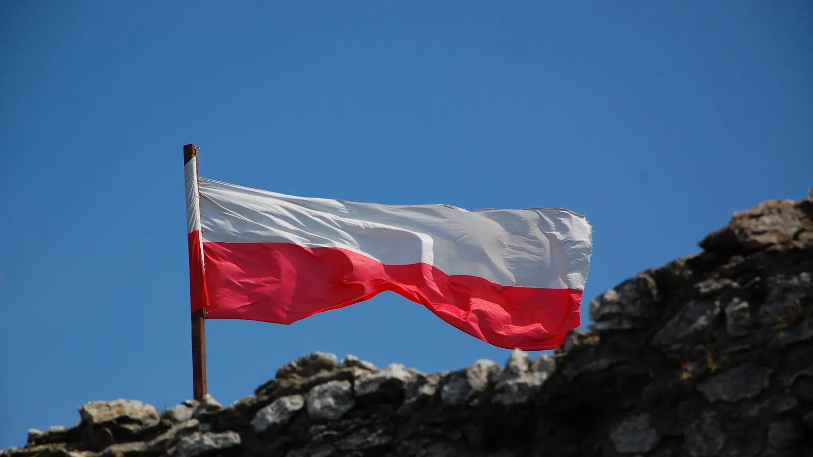 Biało-czerwona flaga na maszcie nad ruinami zamku Ogrodzieniec, na tle błękitnego nieba