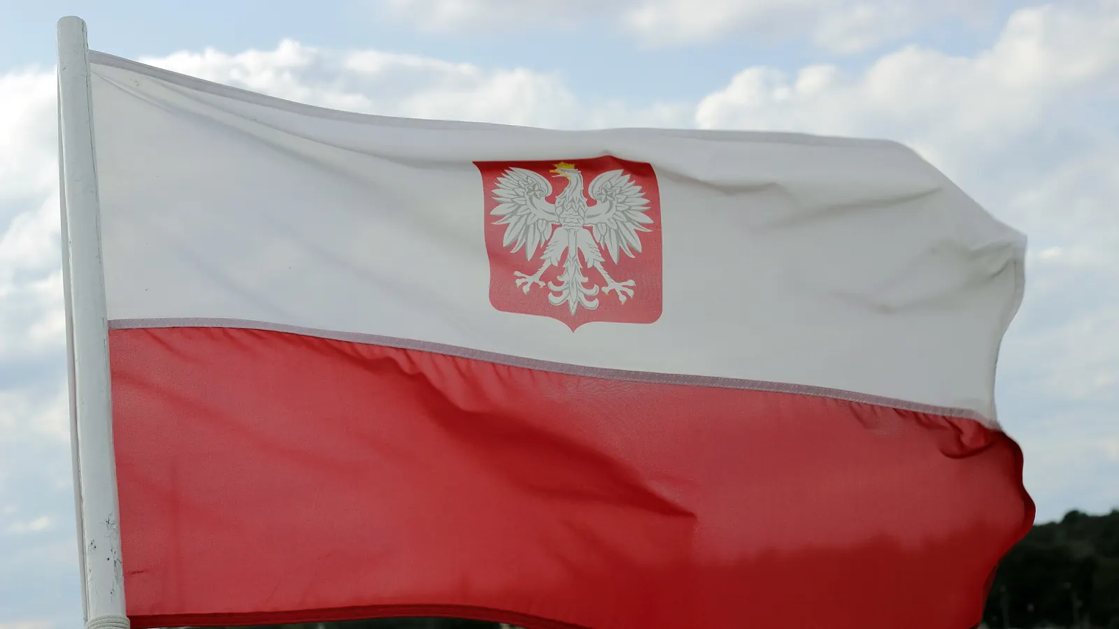 Biało-czerwona flaga z godłem Polski powiewająca na wietrze