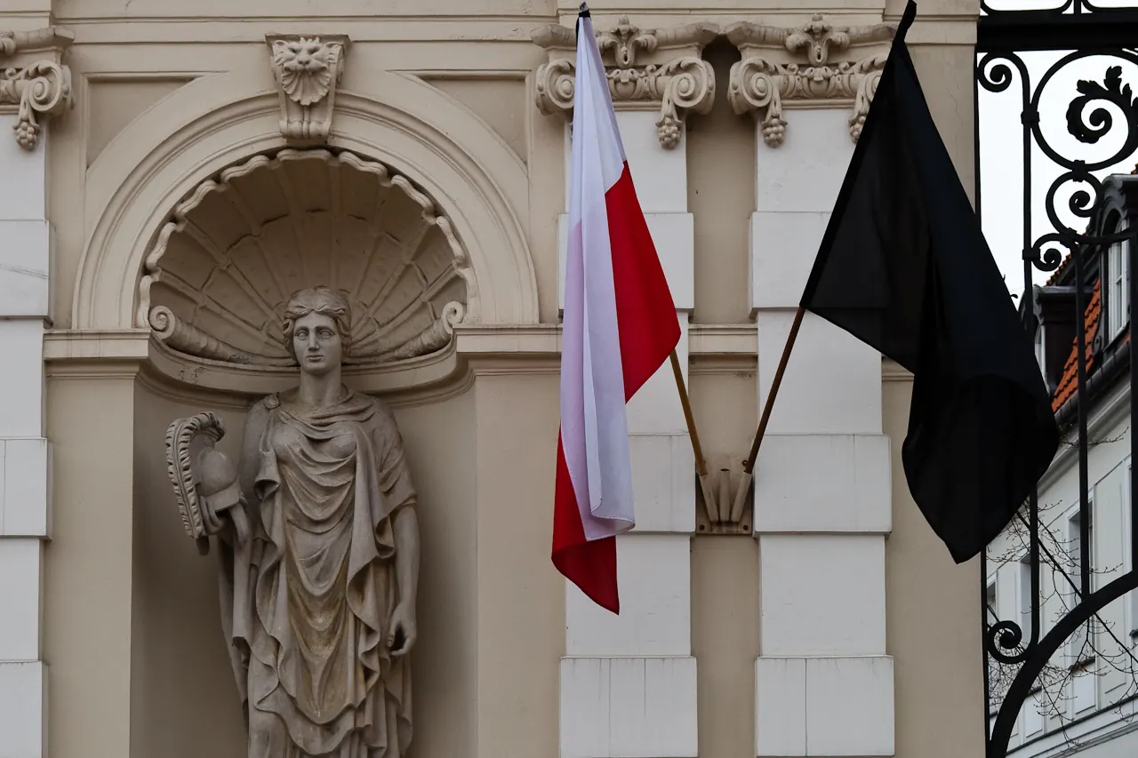 Flaga Polski i czarna flaga żałobna na drzewcach na fasadzie budynku