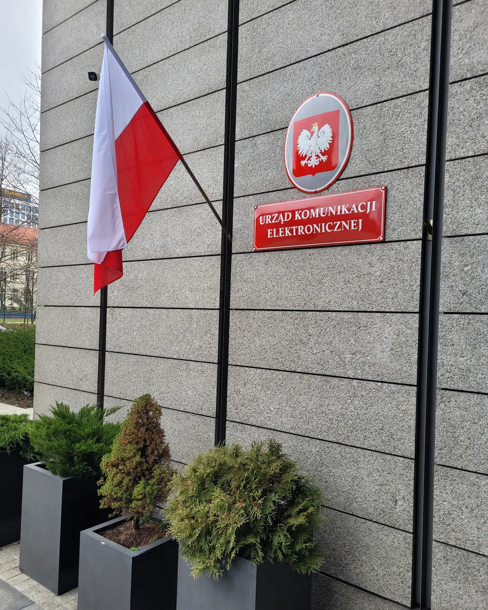 Flaga Polski w uchwycie obok tablicy urzędu z godłem w Warszawie