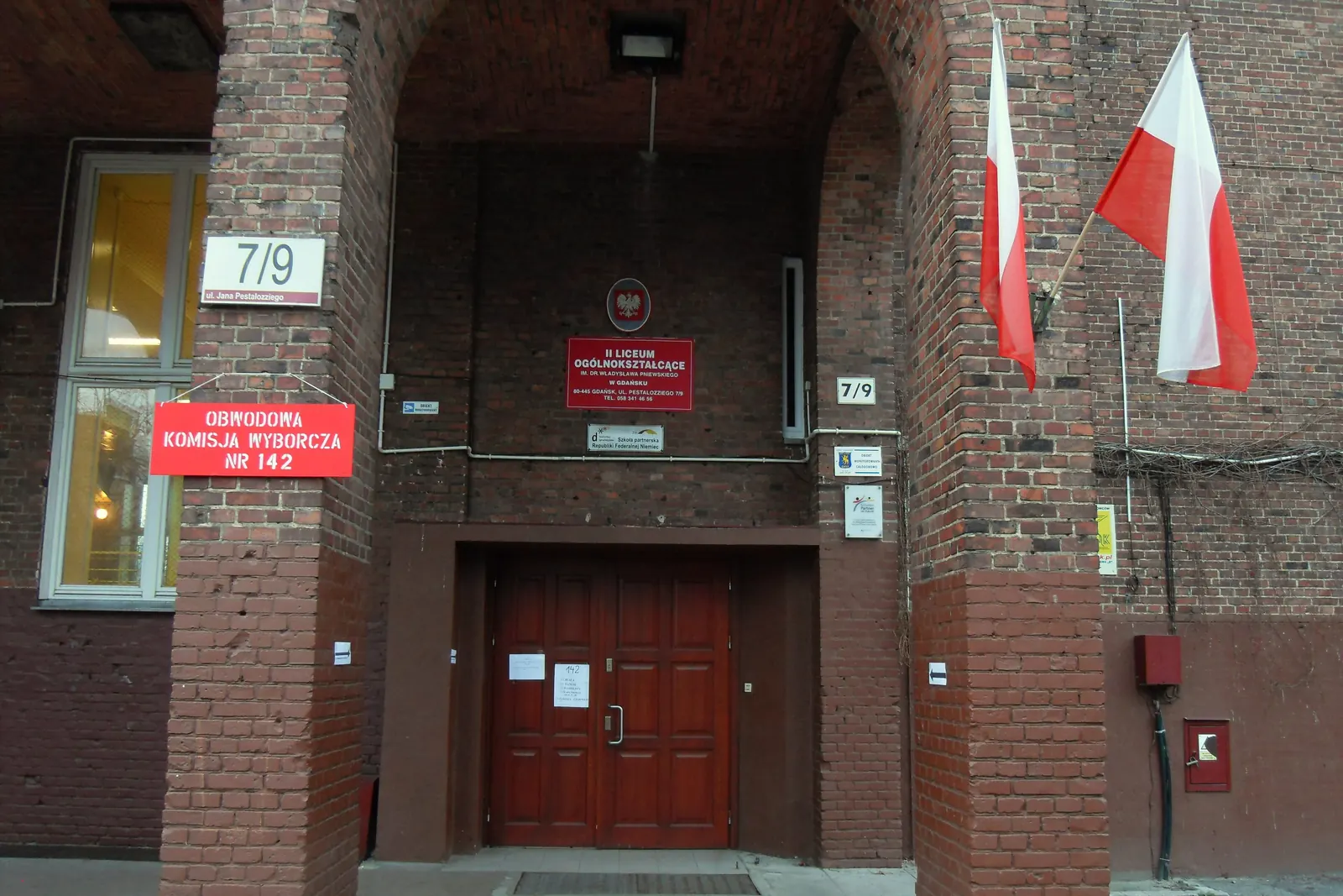 Dwie flagi Polski przy wejściu do lokalu obwodowej komisji wyborczej z godłem w Gdańsku