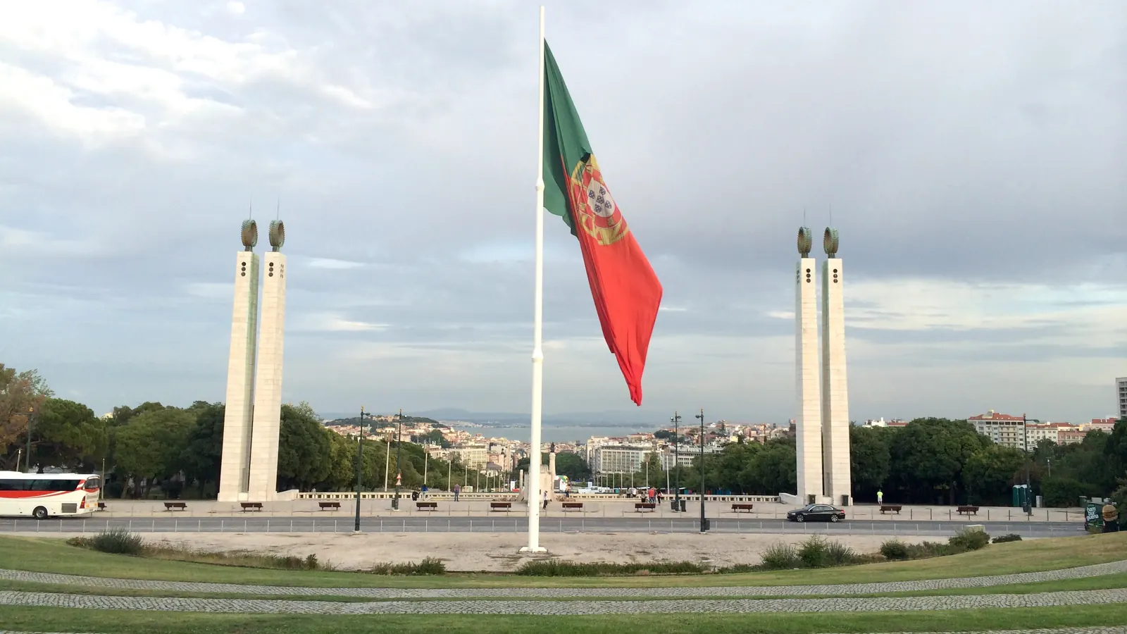 O alto mastro do Parque Eduardo VII com a Bandeira Nacional, entre os dois pilares, com Lisboa ao fundo