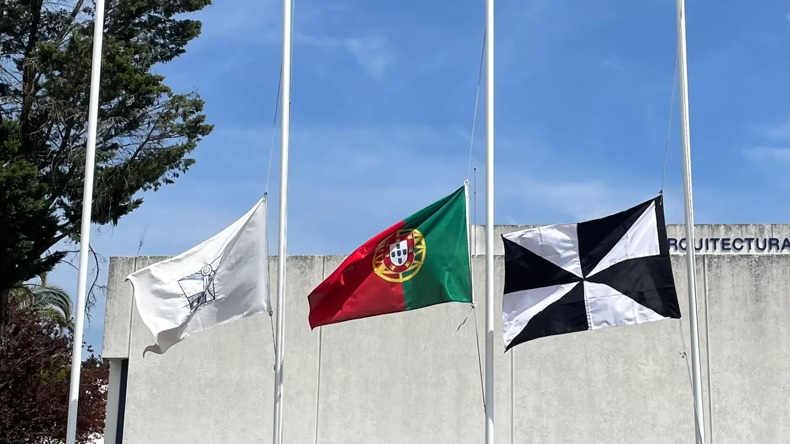 Três bandeiras a meia haste diante de uma faculdade de Lisboa, entre elas a Bandeira Nacional e a bandeira de Lisboa, em setembro de 2025