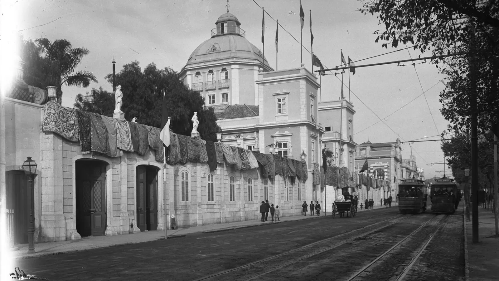 Fotografia antiga de uma rua de Lisboa com o Palácio Burnay embandeirado e elétricos, cerca de 1907