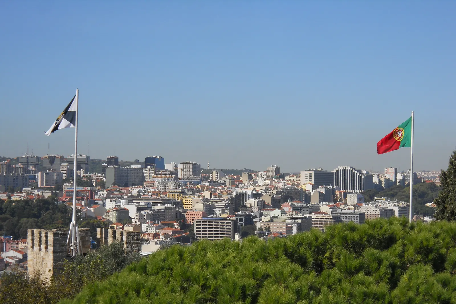 A bandeira de Lisboa e a Bandeira Nacional em dois mastros do Castelo de São Jorge, fotografadas do castelo em direção à cidade