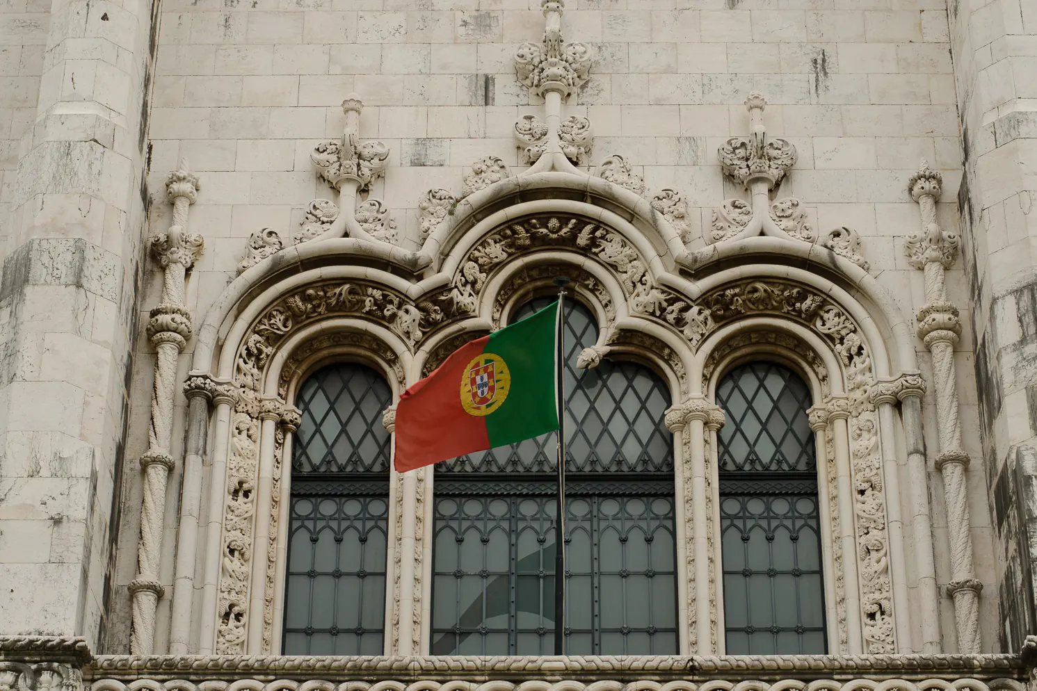 A Bandeira Nacional numa haste diante de uma janela manuelina de pedra lavrada, em Belém