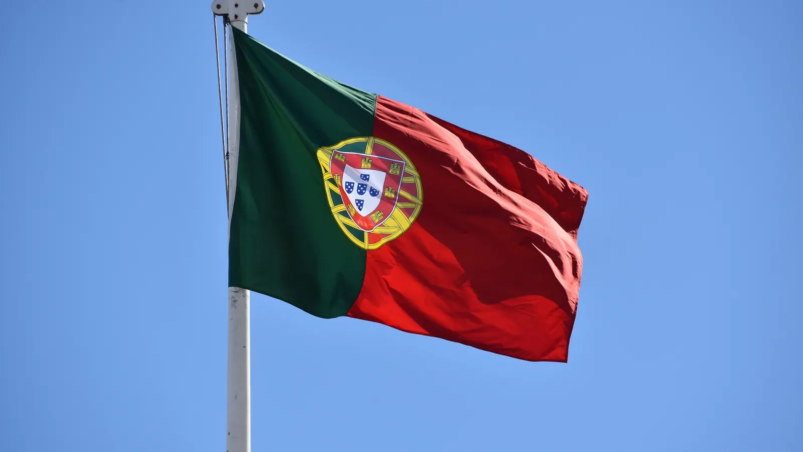 A Bandeira Nacional, verde e vermelha, com a esfera armilar e o escudo, desfraldada contra o céu azul