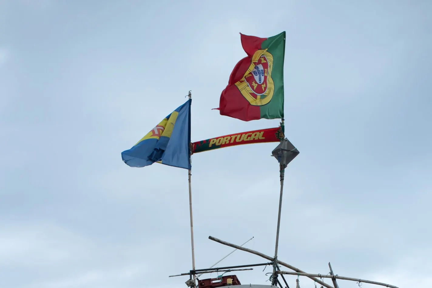O mastro de um barco de pesca em Câmara de Lobos com a bandeira da Madeira e a Bandeira Nacional