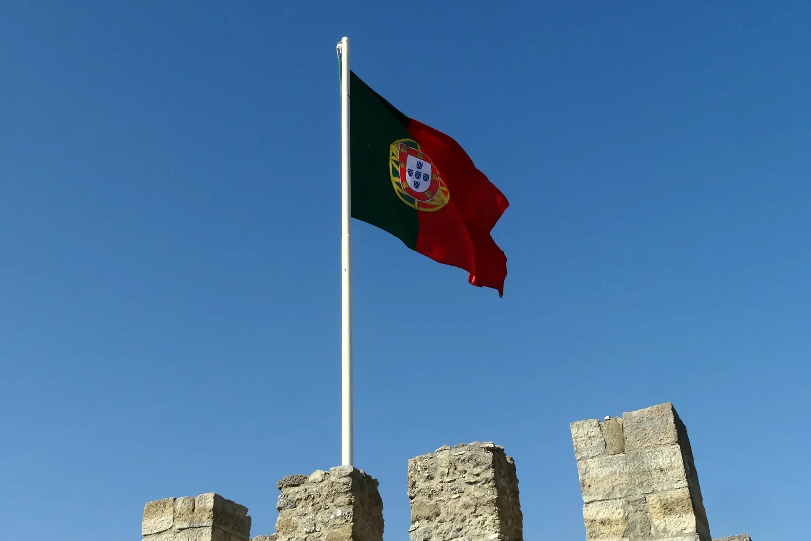 Um mastro com a Bandeira Nacional fixado no alto de uma muralha ameada