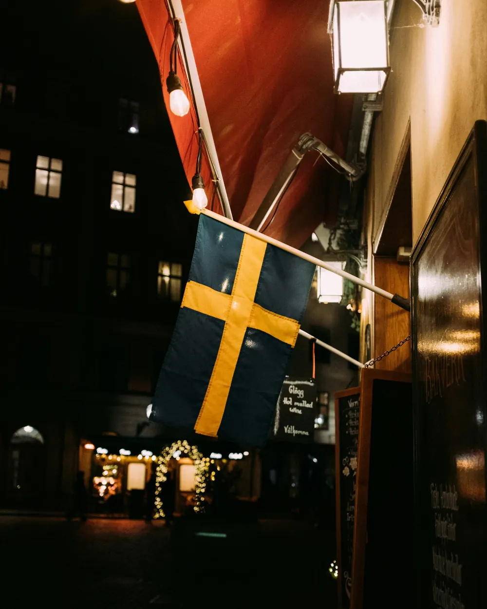 Svensk flagga på en fasad, upplyst av lampor en kväll i Stockholm