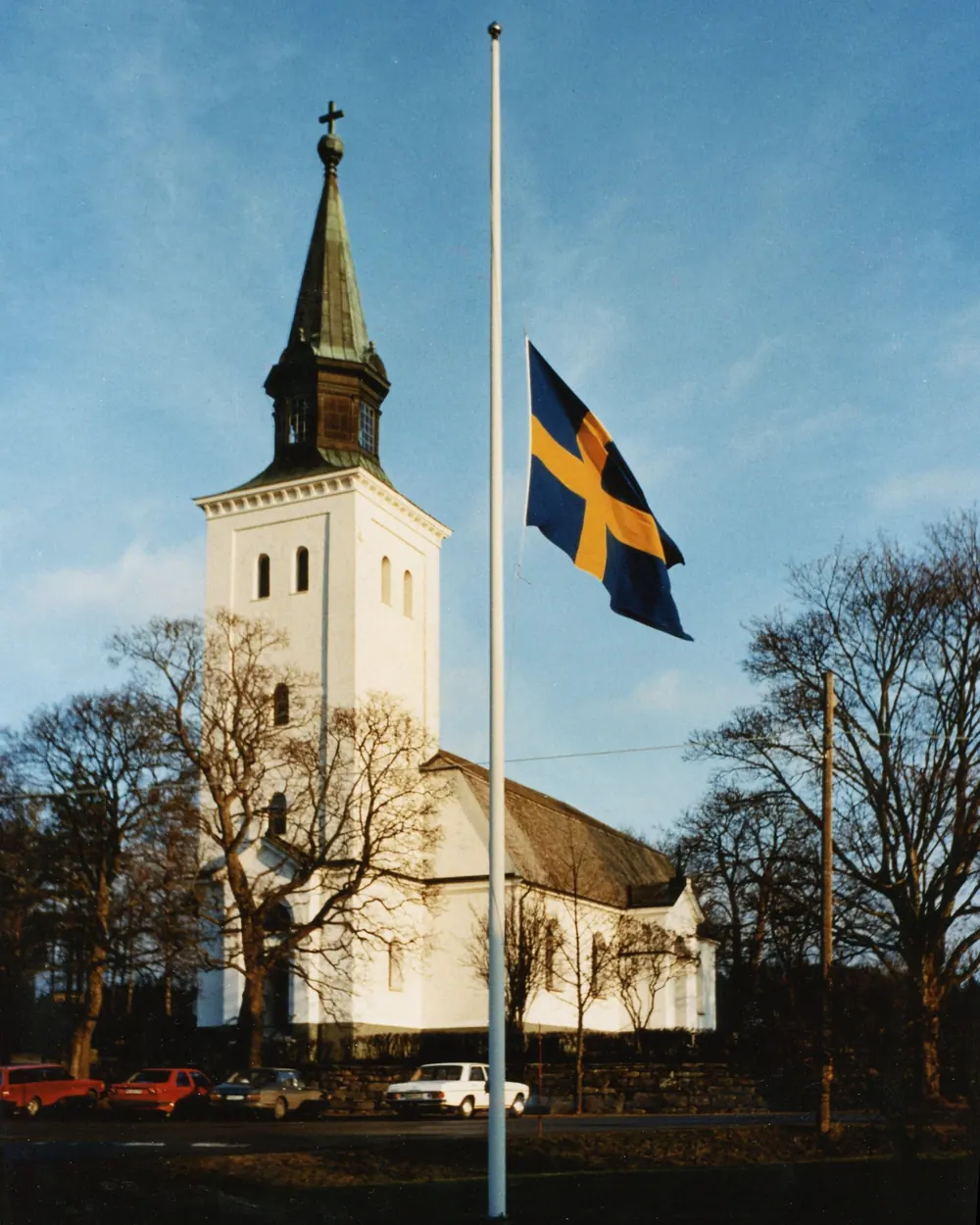 Vit kyrka med en svensk flagga på halv stång framför