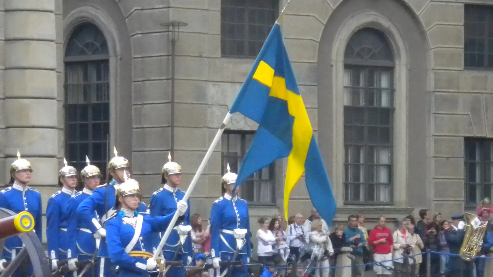 Fanbärare med Sveriges fana vid högvaktsavlösningen, omgiven av vaktsoldater i blå uniformer