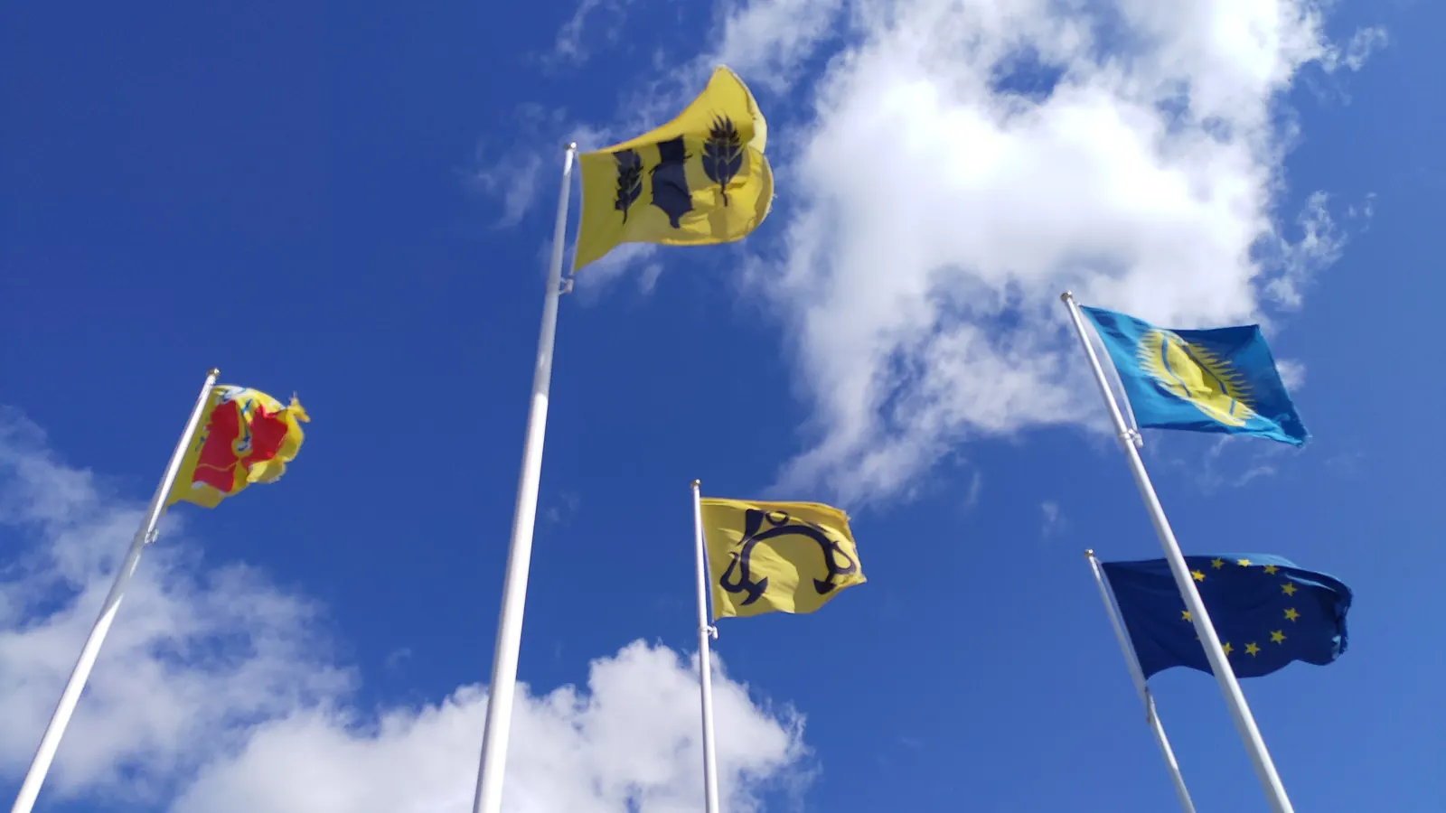 Flera flaggstänger med kommunens flaggor och EU-flaggan mot blå himmel i Strängnäs