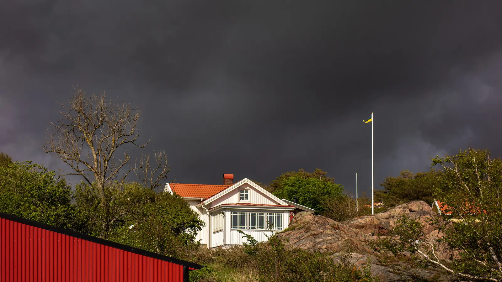 Vit villa på en bergknalle med en flaggstång under mörka regnmoln