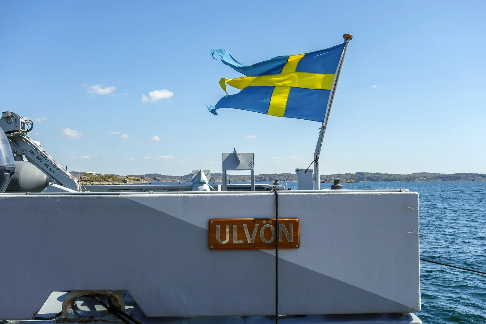 Tretungad svensk örlogsflagga i aktern på ett grått marinfartyg