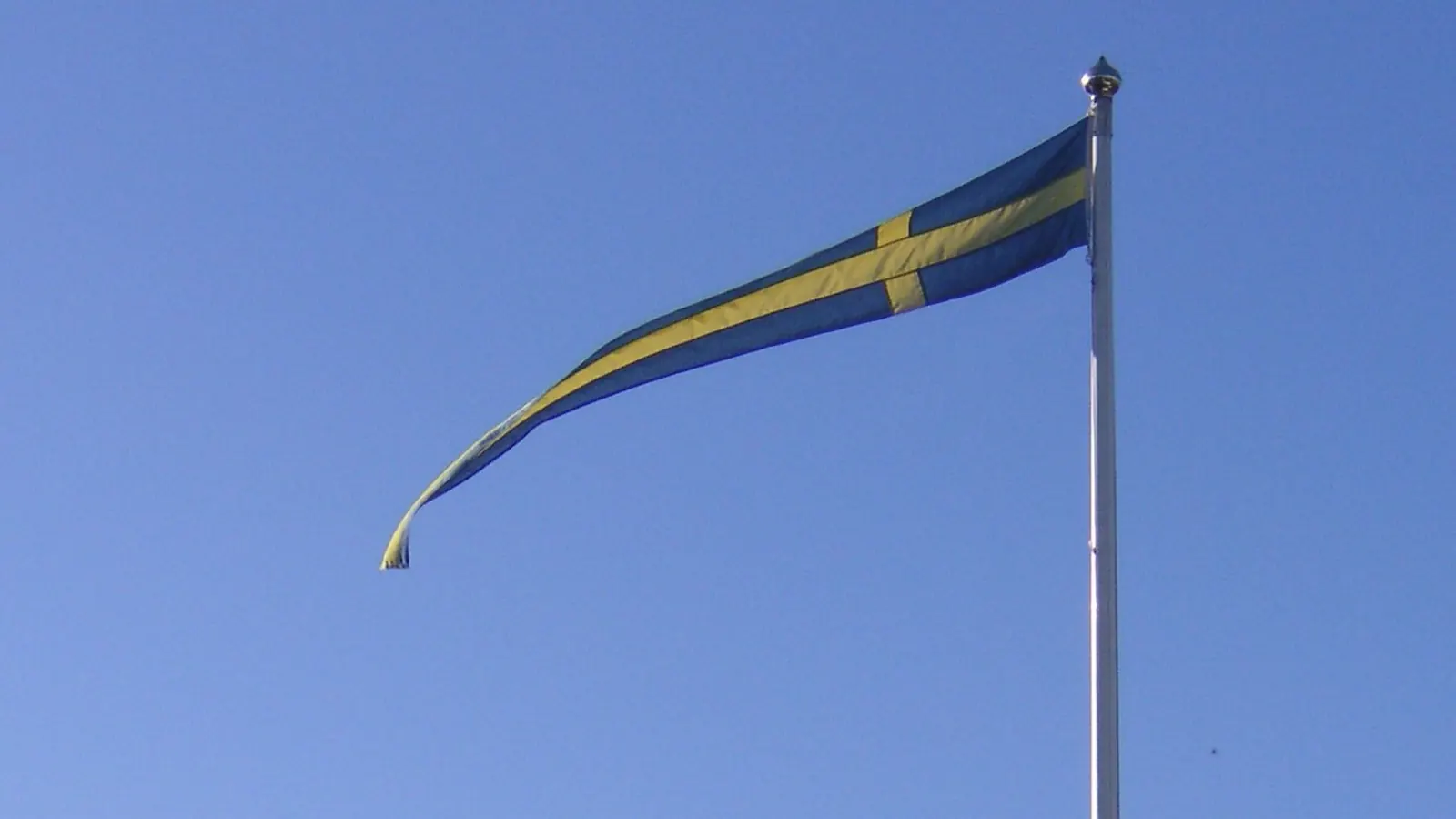 Blå vimpel med gult kors på en vit flaggstång mot blå himmel