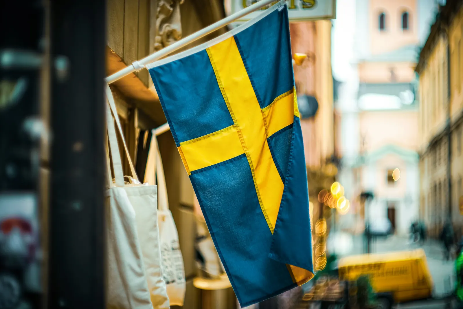 Svensk flagga på en kort stång från en husfasad vid en butiksgata