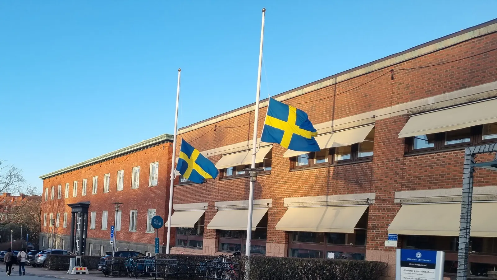 Två svenska flaggor på halv stång framför en tegelbyggnad i Göteborg