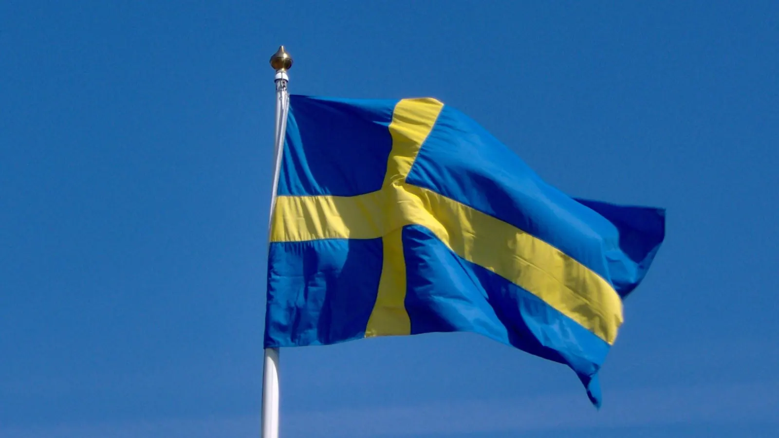 Svensk flagga i närbild på en vit flaggstång mot klarblå himmel
