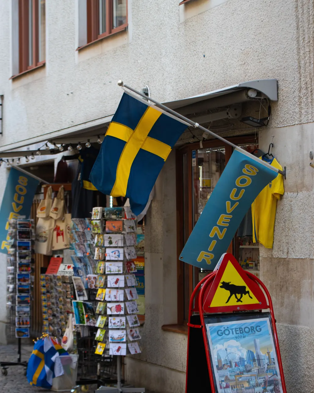 Svensk flagga på en snedstång över entrén till en souvenirbutik med vykort och vimplar