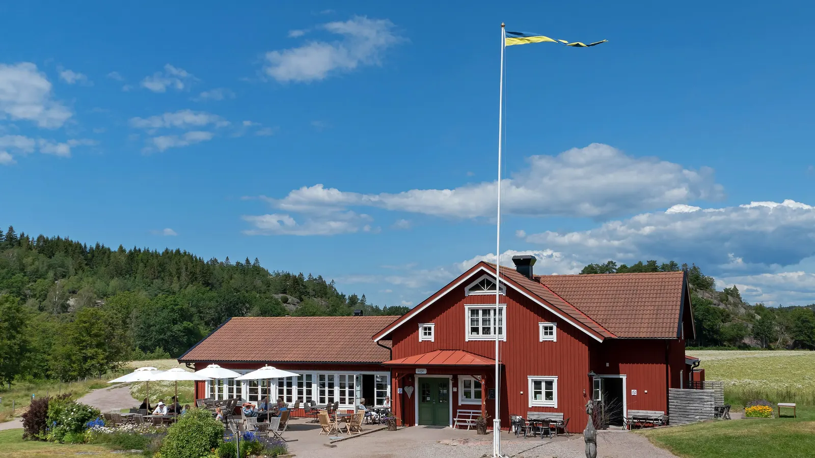Röd gård med uteservering och en hög vit flaggstång med vimpel