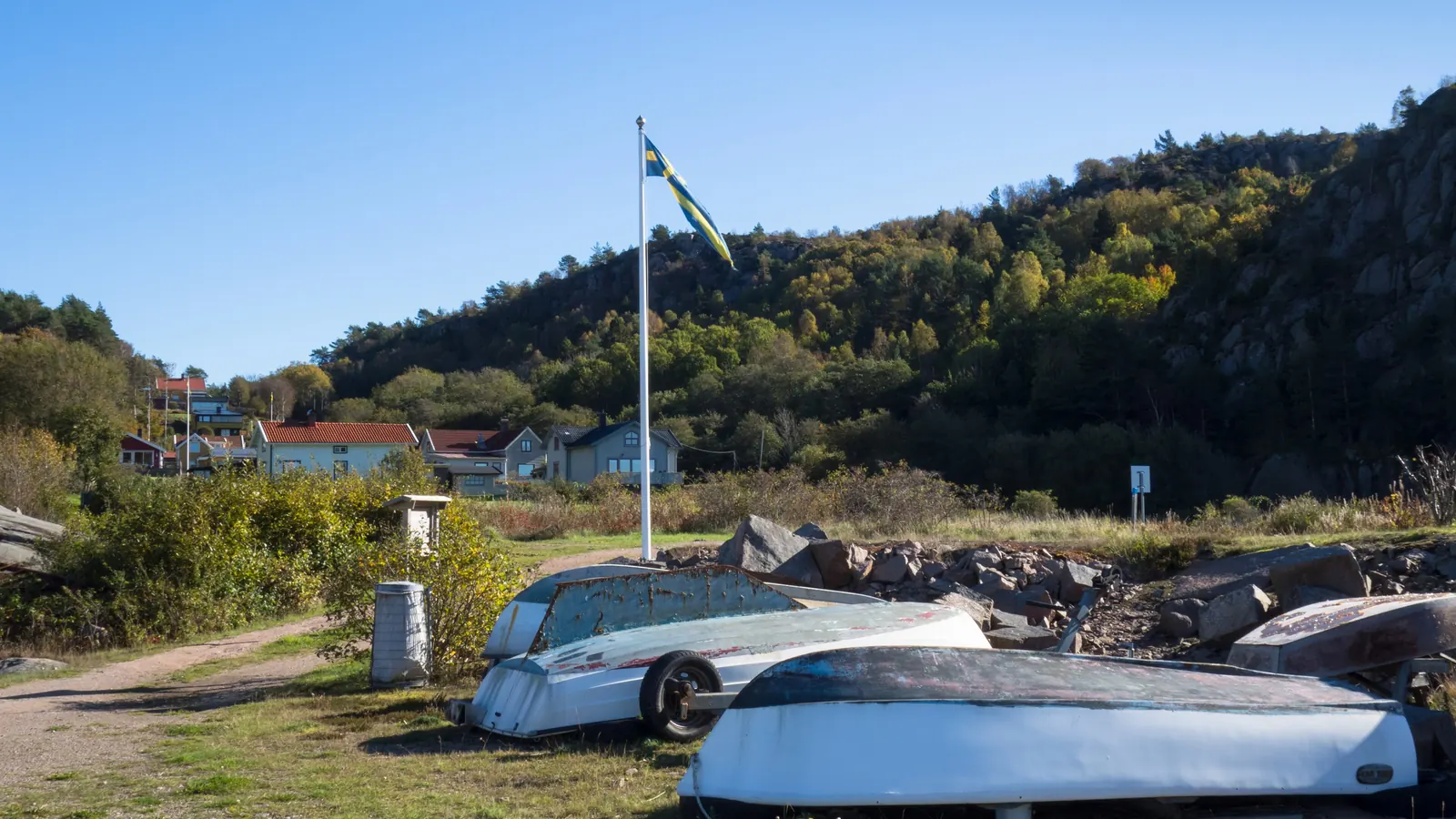 Flaggstång med svensk flagga vid uppdragna båtar i en hamn i Bohuslän
