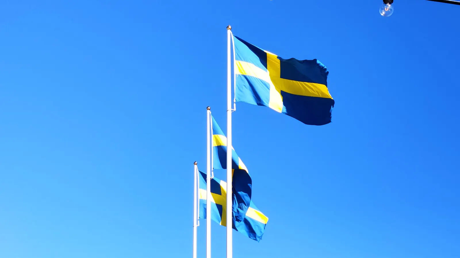 Vita flaggstänger med svenska flaggor mot klarblå himmel
