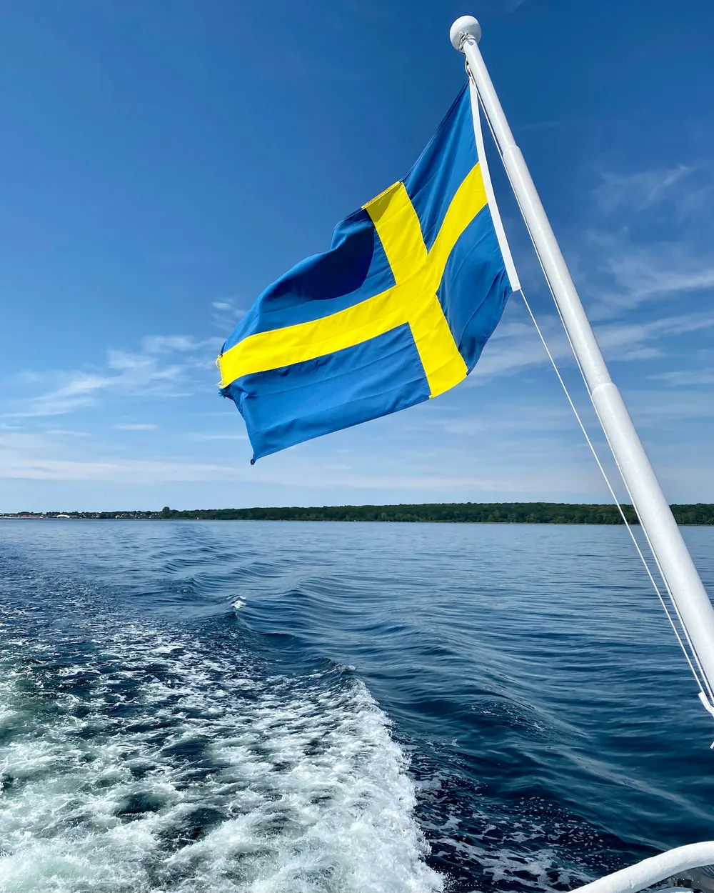 Svensk flagga på en flaggstång i aktern på en båt med kölvatten bakom