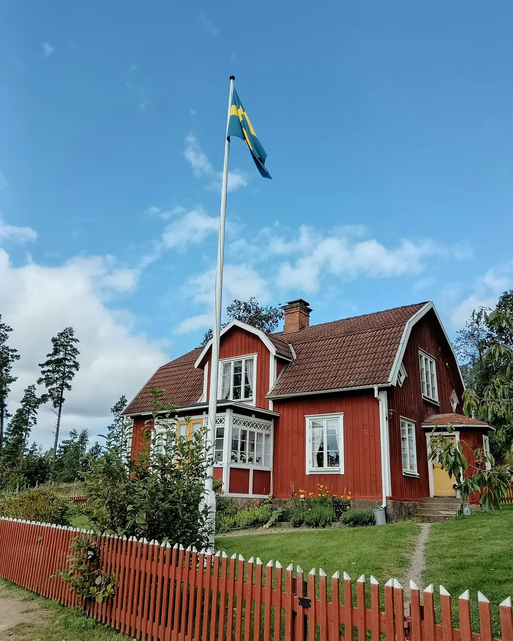 Rött trähus med rött staket och en flaggstång med svensk flagga