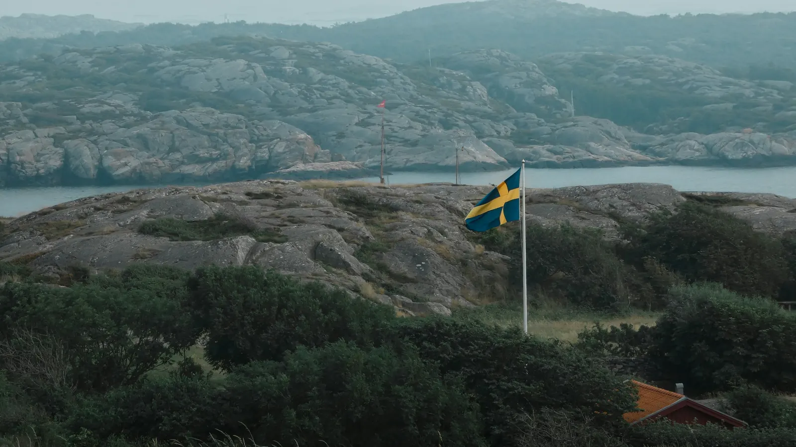 Flaggstång med svensk flagga på en klippa vid kusten en disig dag
