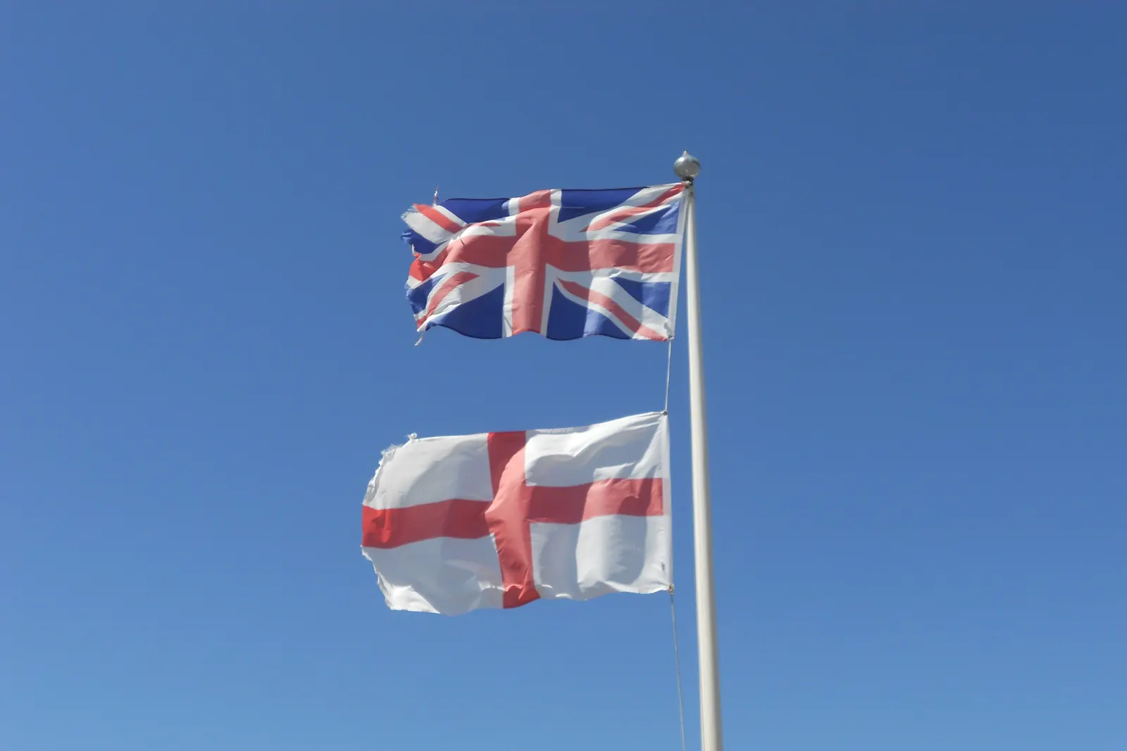The Union Flag above the St George’s Cross on one flagpole against a blue sky