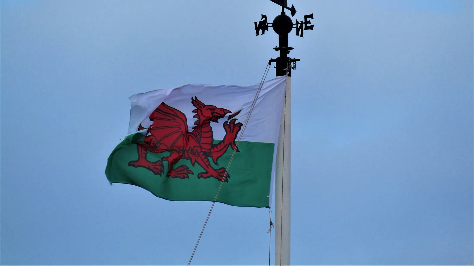 The Welsh flag on a white flagpole with a weather vane