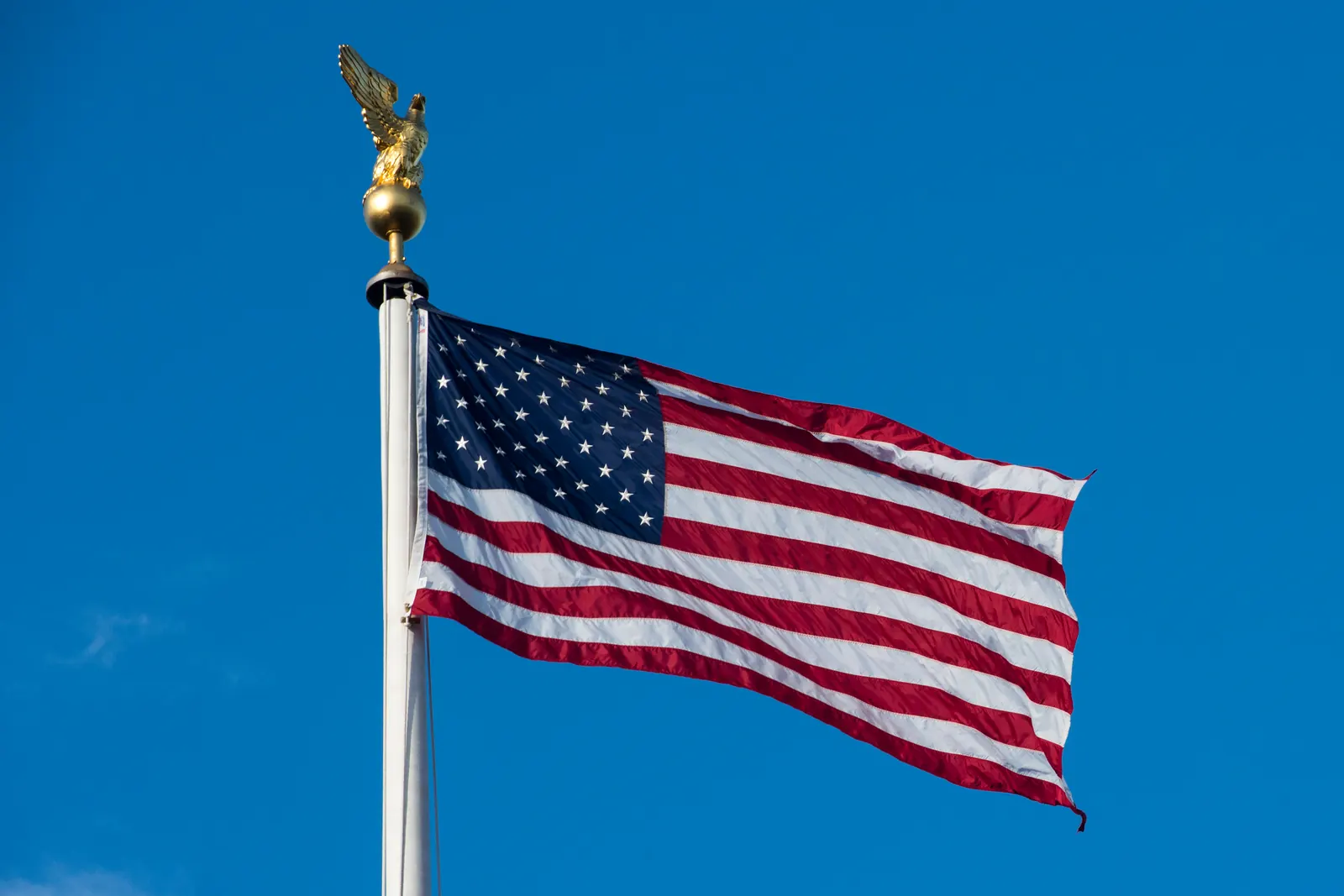 The flag of the United States below an eagle finial against a deep blue sky