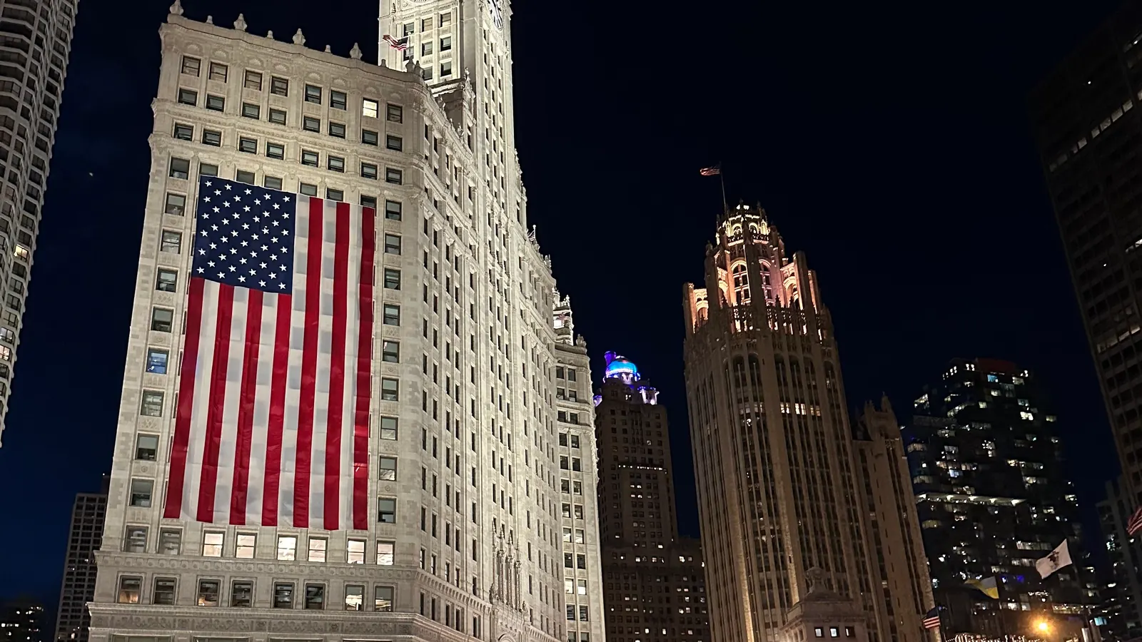 The Wrigley Building in Chicago lit up at night with a large flag of the United States