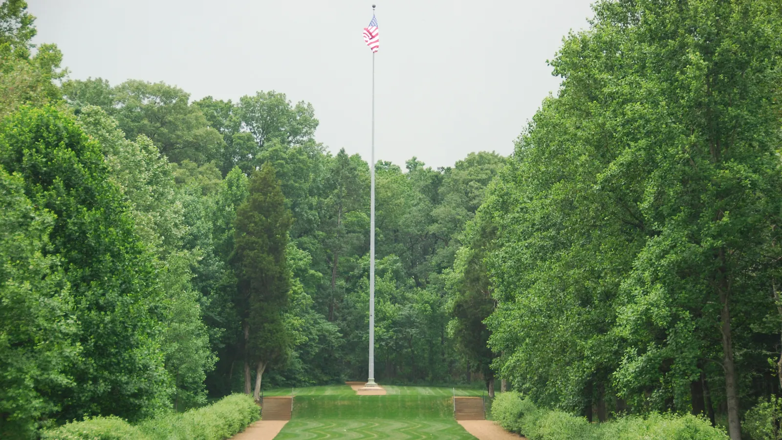 A 120-foot steel flagpole at the end of a tree-lined allée in a national park